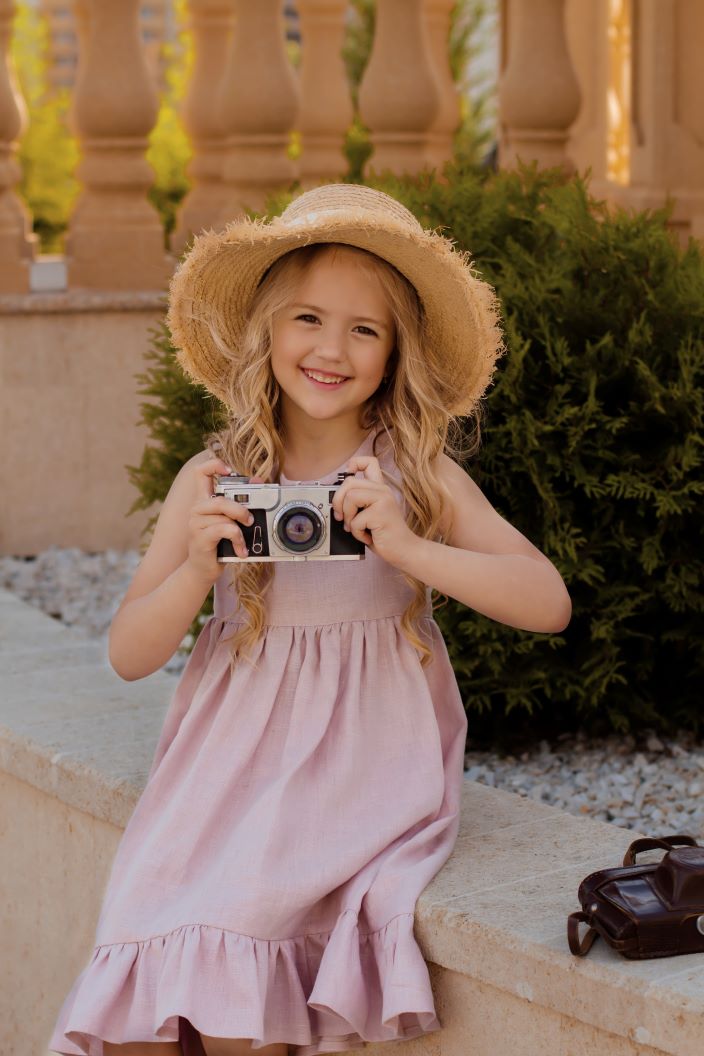 blonde-girl-pink-linen-dress-straw-hat-holds-camera-her-hands 1